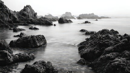 Obraz premium Rocky Seascape with Dark Boulders and Gentle Waves at Dusk in Grayscale