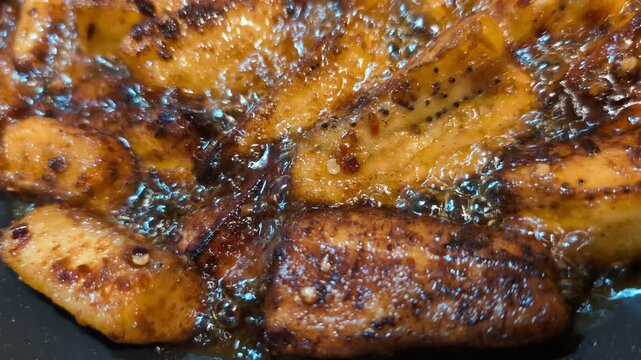 Close up of plantains being deep-fried on black cast iron pan. 
Making patacones