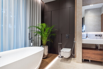 Fototapeta premium Excellent bathroom design with beautiful finishes. A bathtub by the window, a potted palm tree, stylish lighting.