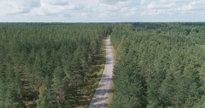 Aerial view of paved two-lane road cutting through a dense pine forest landscape in cloudy summer weather, Harparskog, Hanko, Finland.