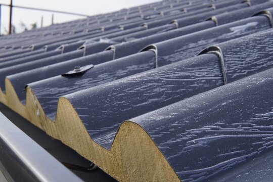 Roofing sandwich panels. Installation of insulated metal sandwich panels. Top view of anthracite-gray metal roofing panels with a tile texture. Bolts with EPDM washers.