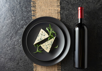 Bottle of red wine and blue cheese on a black plate.