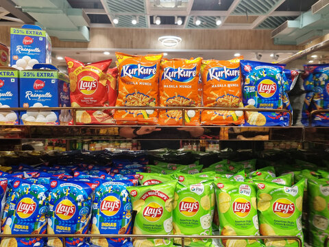 Packets of packaged chips hanging from a shelf in a shop showing Kurkure, lays pringles the most popular brands sold in India