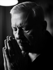 Black and white portrait of a thoughtful senior man in prayer or deep contemplation, hands clasped, conveying hope, spirituality, and reflection with dramatic lighting.