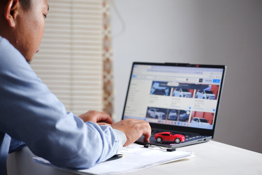 Buying and selling cars online. A man wants to buy a used car. He's browsing through numerous used car listings online on his laptop to compare prices. Many automobiles with picture detail.

