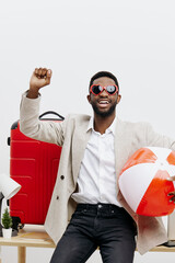 Happy cheerful man with dark skin wearing stylish sunglasses holding inflatable beach ball and red...
