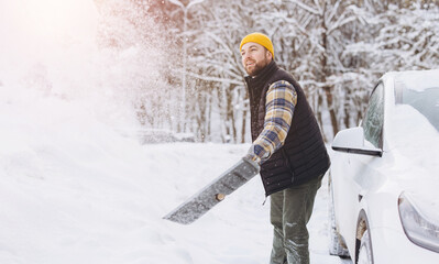 Man actively clearing snow from a residential driveway next to a white car during cold winter weather