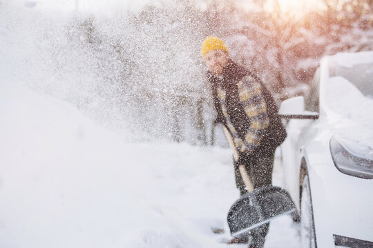 Man clearing heavy snow with a shovel from a driveway parking spot beside his car on a cold winter morning, outdoor chore