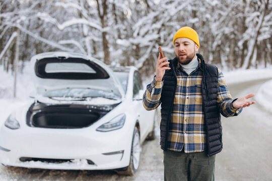 Frustrated man calling for roadside assistance during electric car breakdown in snowy winter forest