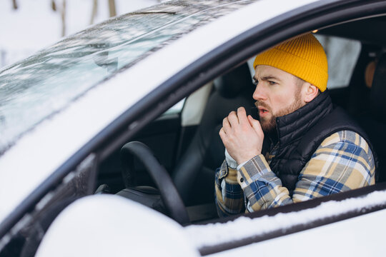 Man feeling cold and warming hands inside car during winter weather. Experiencing a breaking down car or cold start issue