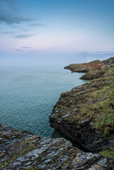 Vertical view of Wicklow Head cliffs at twilight, rugged rocks and teal sea under soft lavender sky, showcasing coastal solitude