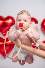 Fototapeta premium Cute smiling malshy in a Cupid costume on a white background with a bow and arrow in the shape of a heart. Happy Valentine's Day concept.
