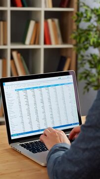 Person typing on a laptop with financial data displayed on the screen, in a home office setting