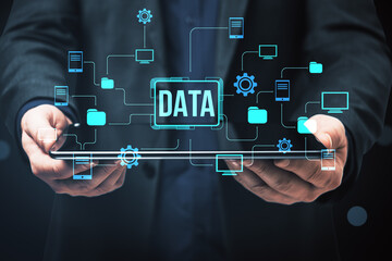Businessman holding tablet with digital data network icons and folders representing cloud computing and data management concept on dark background.