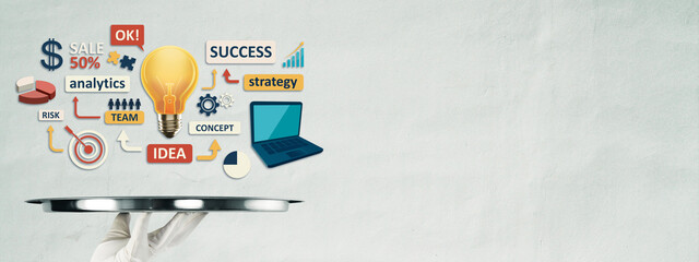 Hand holding silver tray with business symbols including light bulb, pie chart, laptop, and strategy icons on gray background concept of innovation.
