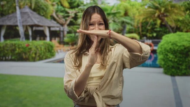 Woman hands forming time out gesture while shielding face at resort pool; pause boundary frustration.