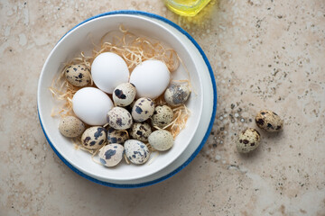 Bowl with fresh uncooked quail and chicken eggs on a beige granite background, horizontal shot, view from above