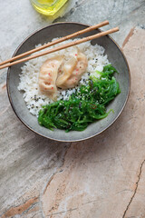 Plate with wakame seaweed, white rice and dumplings on a grey and roseate granite background, vertical shot with space, above view