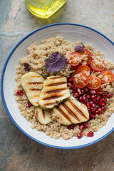 Quinoa with grilled halloumi cheese, cherry tomatoes and pomegranate in a white and blue plate, vertical shot, middle closeup