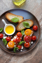 Roasted tomato bruschettas with ricotta and fresh basil, vertical shot on a brown granite background, elevated view
