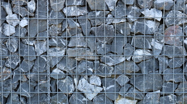 A fragment of a gabion with a metal cage filled with large gray boulders, the hard, solid texture of stone and metal, a view of a finished gabion with natural rock filling behind an iron grate