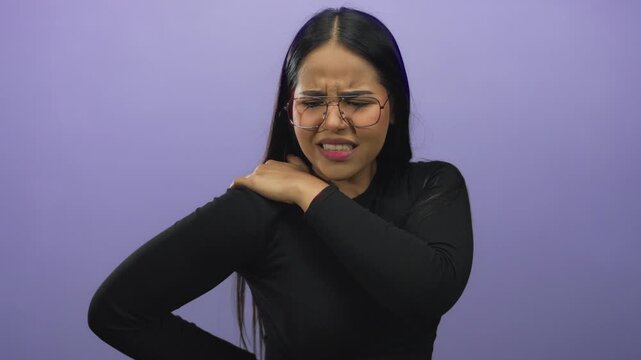 Woman in glasses massaging her shoulder in discomfort, isolated against a purple background, expressing pain relief needs. - Powered by Adobe