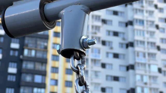Empty metal swing moving back and forth at a playground. A detailed close up view of the chain and attachment against an urban building