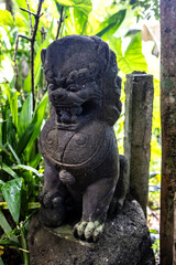 Traditional Balinese stone guardian lion statue displayed in a lush garden setting in Ubud, Bali, Indonesia. The sculpture represents protection and spiritual symbolism in Balinese Hindu culture.