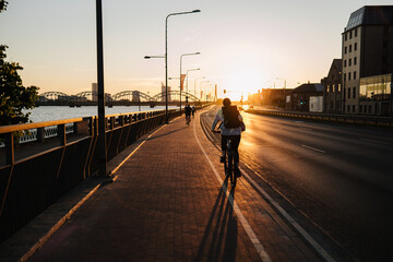 young woman riding a bike on a city bike lane  at sunset
