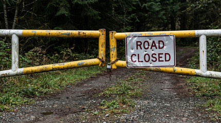 Road closed barrier with warning sign in forested area  