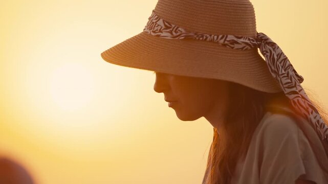 Family time at the beach during sunset with a woman in a hat enjoying the view and sharing moments on a warm evening