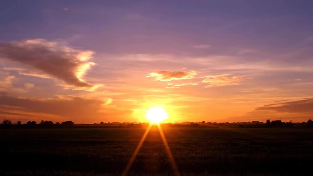 Sunset over open landscape with glowing sun near horizon and warm sky colors. Peaceful natural scene shows calm atmosphere, light rays and tranquil countryside view.