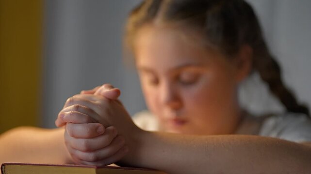 Close-up praying child hands. Bible under hands while girl focuses worship. Child remains silent in moment worship. Gentle fingers locked show inner focus. Worship calm child stillness blend together.