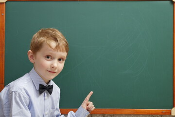 A cunning elementary school student has something in mind while standing at the blackboard and demonstrates it with a hand gesture.