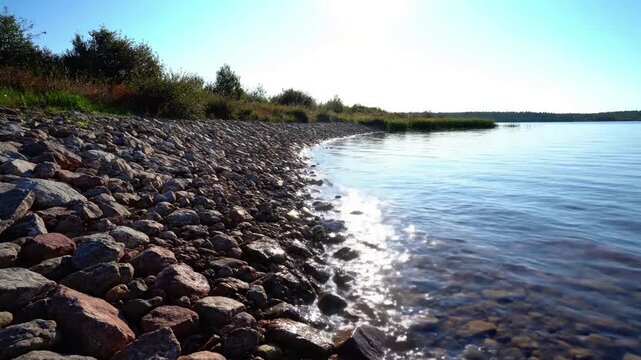 Morning Glint on River Riprap A wide, stable shot of a river bank, with the low morning sun creating long shadows and golden glints across wet riprap stones as the water gently laps the shore.