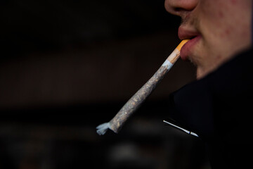 Side profile close-up of a person holding an unlit hand-rolled cigarette between the lips. Dark background with shallow depth of field. No smoke visible.