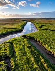 Meandering stream cuts through verdant marshland under a blue sky with wispy clouds in golden light