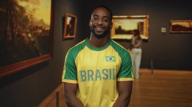 Man smiling in a yellow brazil jersey showing a flag while standing in a modern gallery building; pride.
