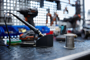 A soldering iron is resting on a worktable with a soldering iron and solder