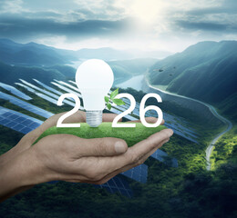 2026 white text and led light bulb with fresh leaves on green grass in hands over solar photovoltaics cell farm on mountain in sunny day, Happy new year 2026 green ecology and saving energy concept
