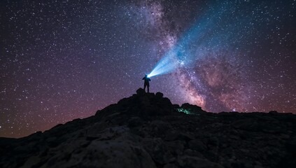 Hiker silhouette on rocky summit with headlamp beam pointing left