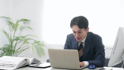 オフィスでPCを使って作業しながら悩む男性ビジネスパーソン