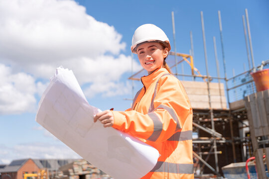 Portrait of young woman site manager  performing construction site inspection while holding plans and drawings
