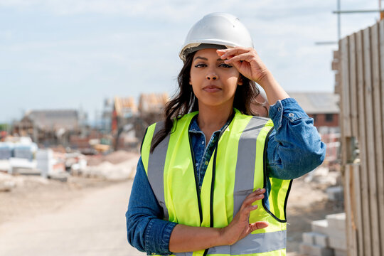 Portrait of young woman construction worker in safety gear standing confidently on building site