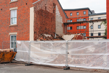 Building demolition in urban area with construction barriers and nearby structures