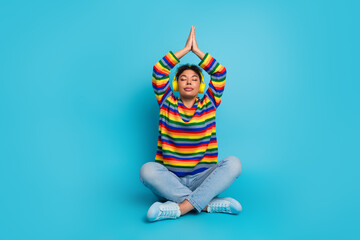 Young woman in colorful striped sweater meditating with headphones against blue background promoting style relaxation wellness fitness fashion