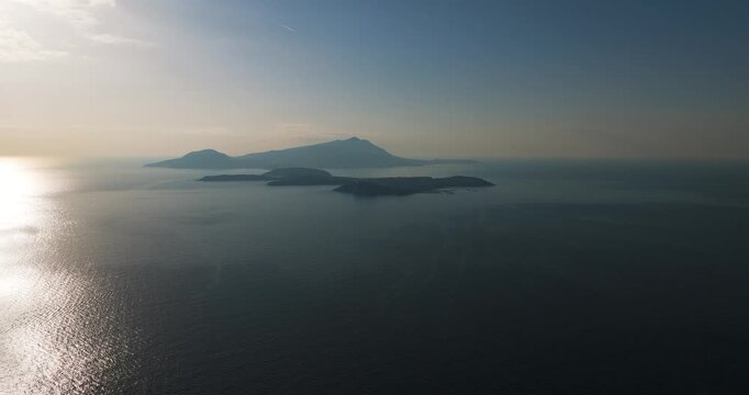 Aerial view of Ischia and Procida islands surrounded by the tranquil sea, with the sun's rays creating a shimmering effect on the water, Capo Miseno, Campania, Italy.