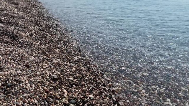 Waves interact with pebbles at the shoreline under sunlight. Water moves smoothly while creating natural patterns near the shore.