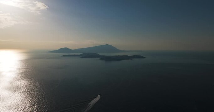 Aerial view of the dark blue sea surrounding the Ischia and Procida islands under a bright sky, with a boat sailing away, Capo Miseno, Campania, Italy.