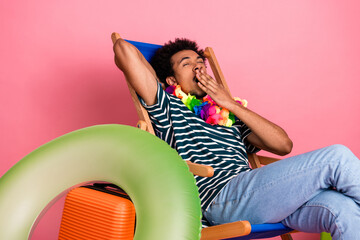 Young mixed race man relaxes in a colorful chair with a flower lei and pink backdrop for a vibrant casual summer lifestyle stock image